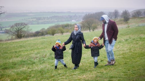 A family of four walking hand in hand on a grassy field